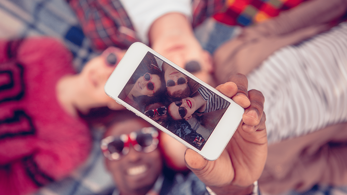 Henkilöitä makaa maassa, yhden käsi ojentuu ottamaan heistä selfietä